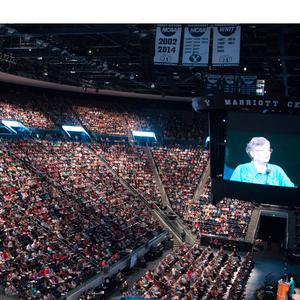 2016. No Marriott Center são realizadas as sessões da conferência de mulheres da BYU, que teve início em 1976. A fotografia de Sandra Rogers, vice-presidente internacional da BYU, aparece no telão.