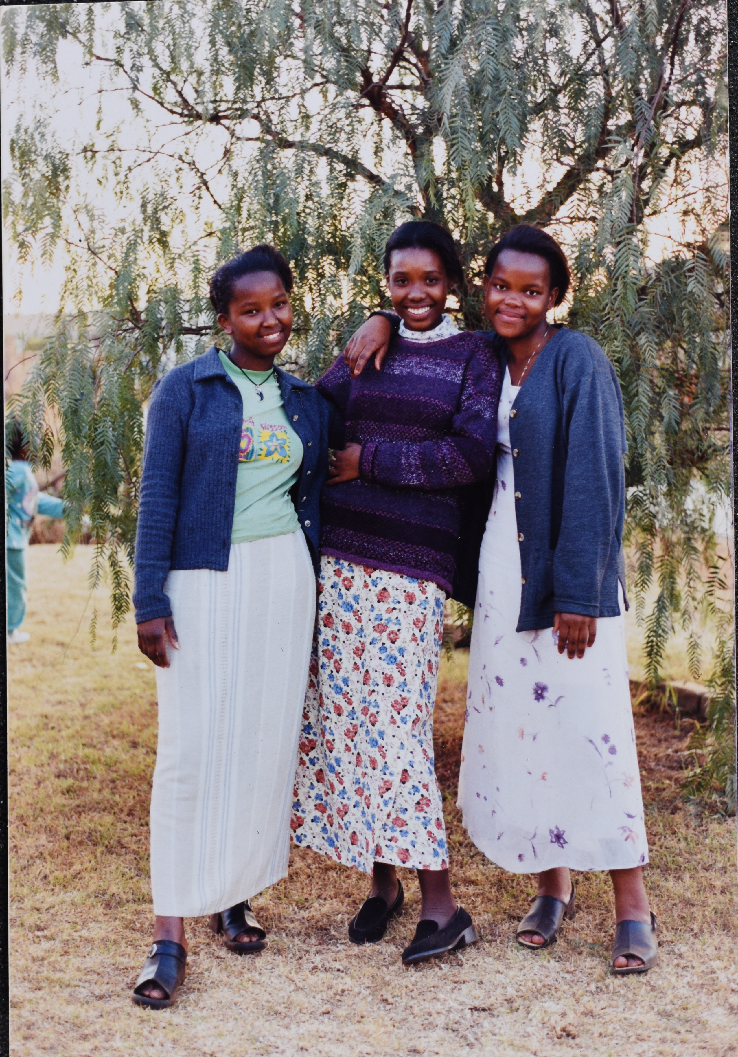 <strong>Zandile Qinisile after Sunday church meetings, South Africa.</strong> Circa 1998. Zandile (left), her cousin Zamanguni Queeneth Dlamuka (right), and friend Yolanda Radebe (center) lived in Protea Glen, Johannesburg, and attended church together. The young women often returned from church to Yolanda’s home to sit under the tree, where they chatted and discussed church activities. (Image courtesy Zandile Qinisile.)